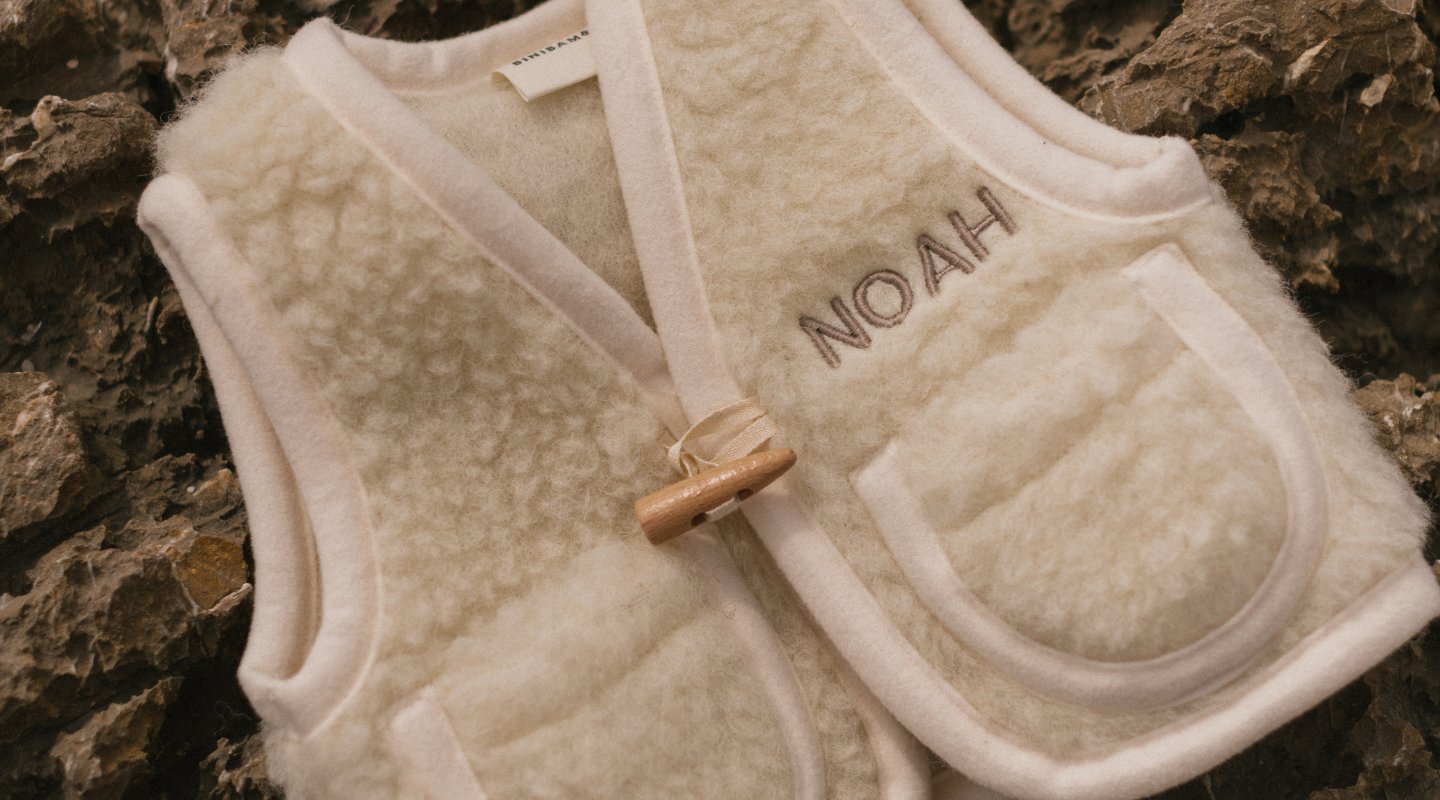 PERSONALISED SHEEPSKIN PRAM LINER IN MILK COLOUR. CHILD WEARING BRUNO BROWN GILET